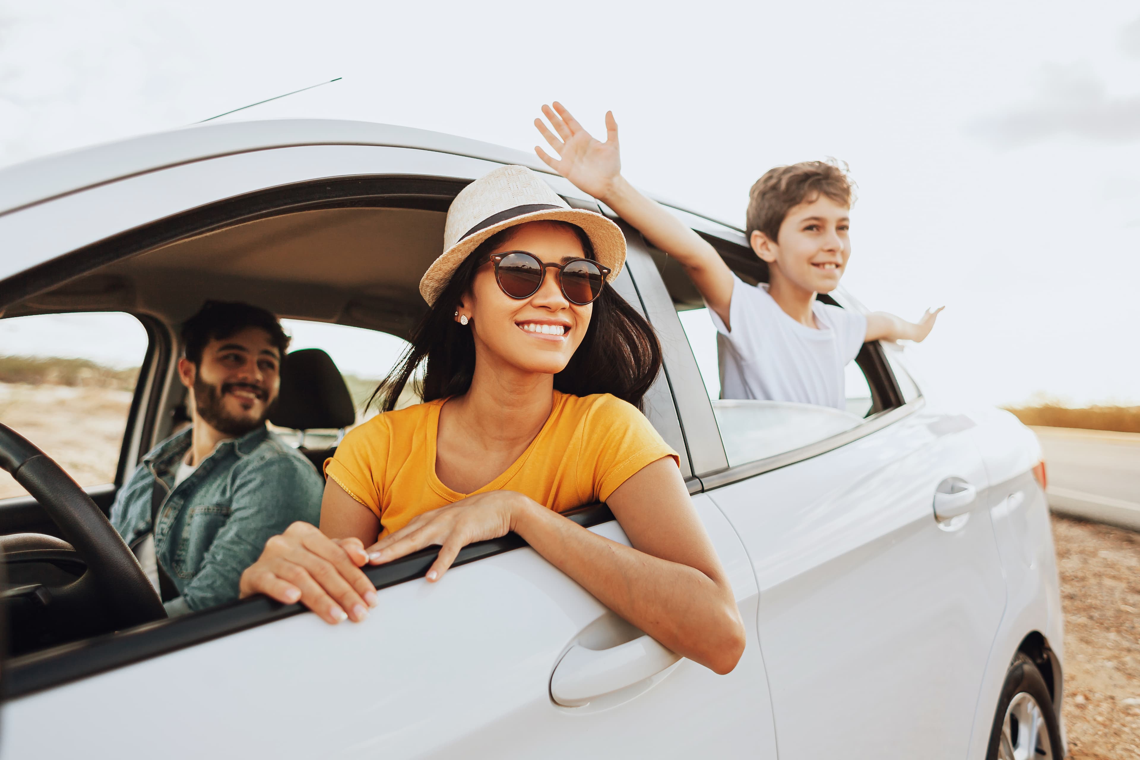 A family on a road trip, smiling from their car